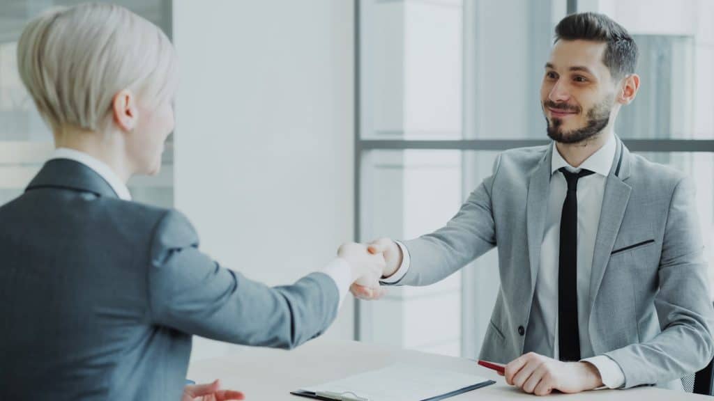Two professionals shaking hands across a table in a modern office, representing a local phone installer who shows up in person