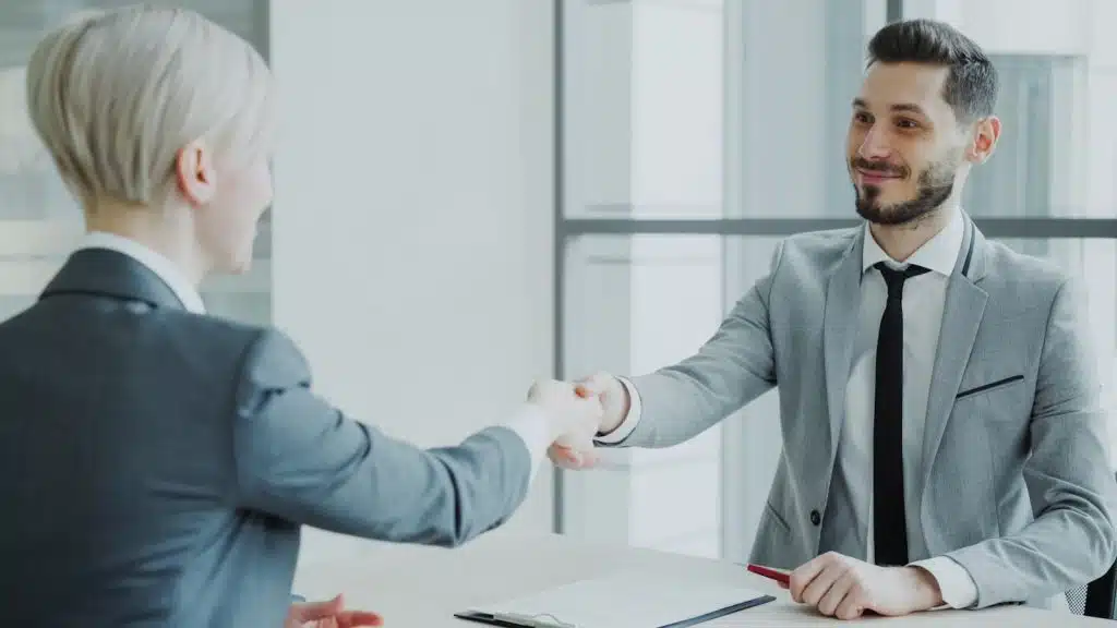 Two professionals shaking hands across a table in a modern office, representing a local phone installer who shows up in person