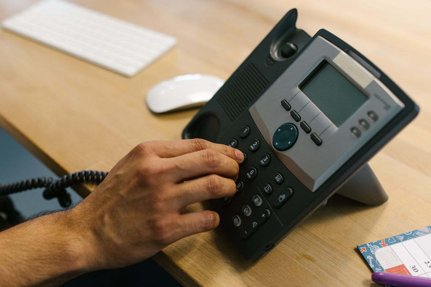 Business professional dialing a modern VoIP desk phone on an office desk