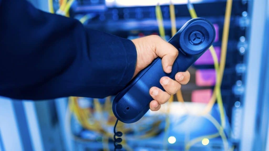 Technician holding a business phone handset in front of network cabling and switch equipment during a business phone system installation